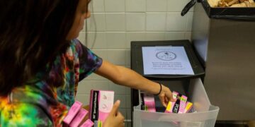 A woman stocks a bathroom with free pads and tampons