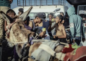 A hungry young boy eats raw noodles as dislocated Palestinians carry the humanitarian aid they have received from a United Nations distribution point in Rafah, southern Gaza Strip on May 27, 2025.